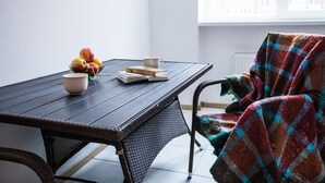 A dining table with fruits, a book, and a cup. A chair with a colorful blanket is partially visible.