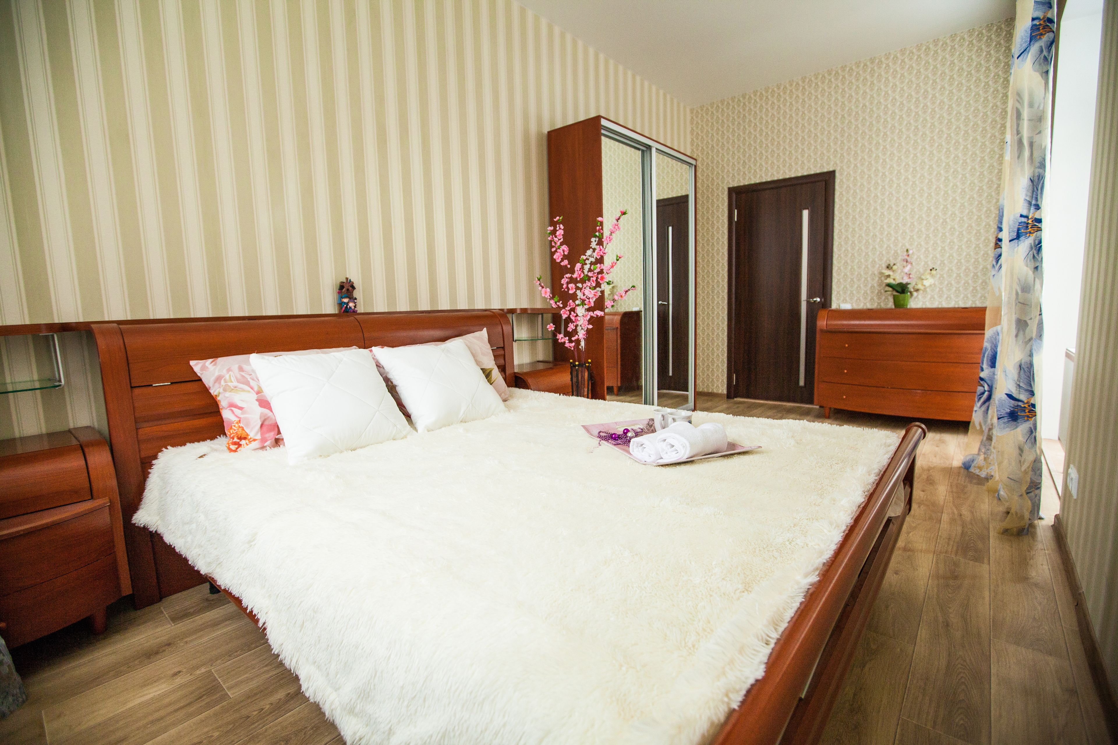 Una cama bien hecha con un cubreblanco esponjoso, cabecera de madera y dos mesitas de noche con cajones.