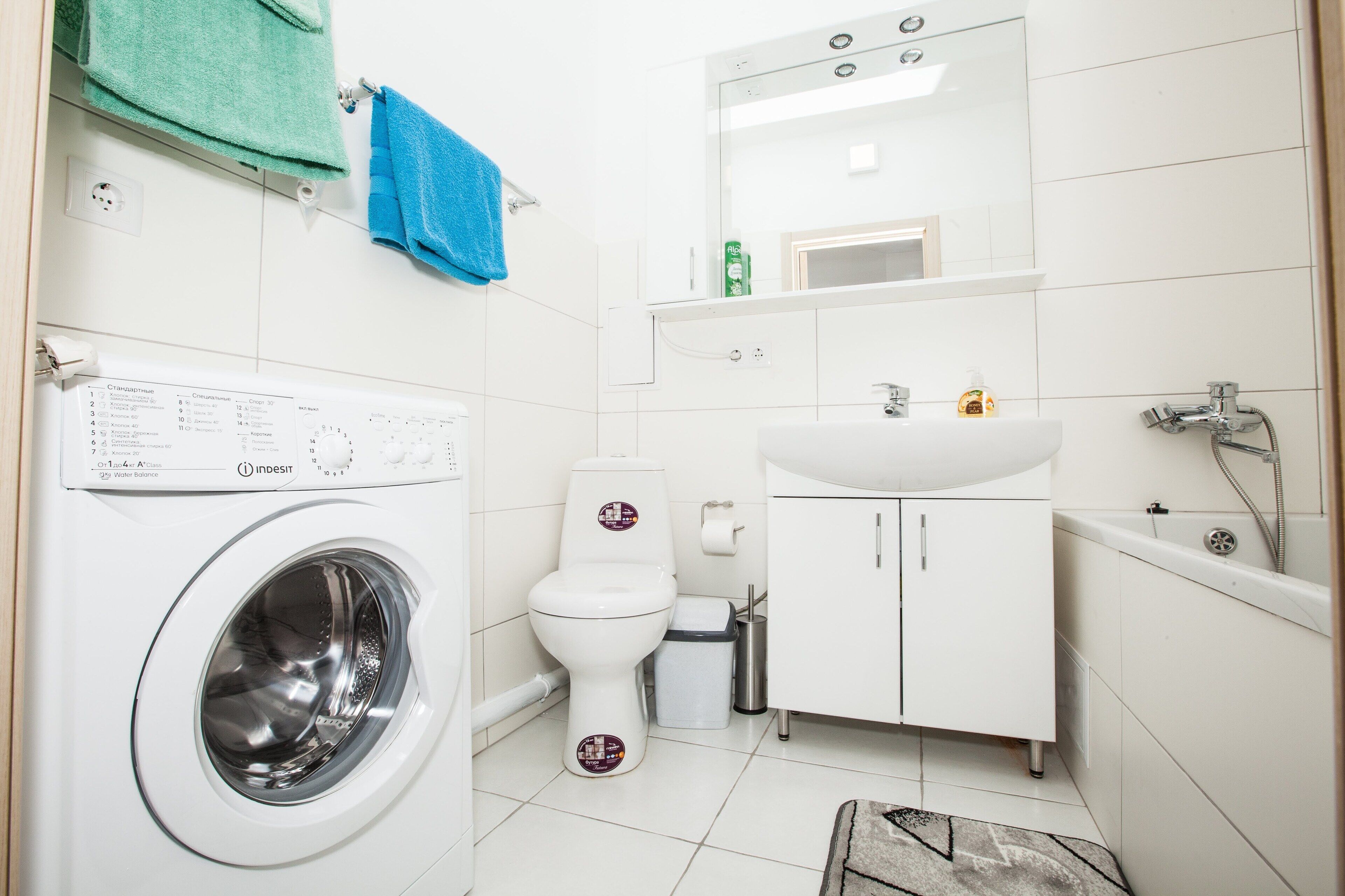 A compact, modern bathroom with a washing machine, toilet, sink, and shower.