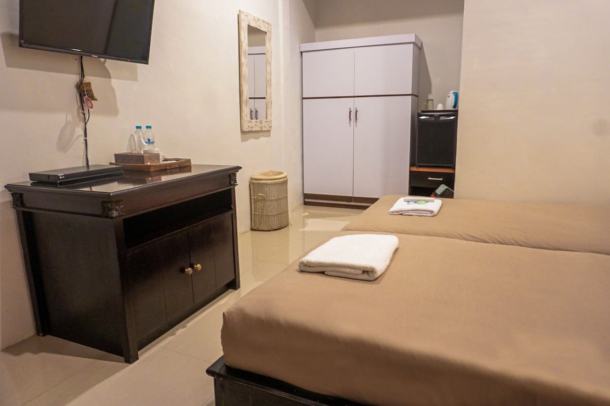 A hotel room with a bed, a dresser, a television, a wardrobe, and a trash bin.