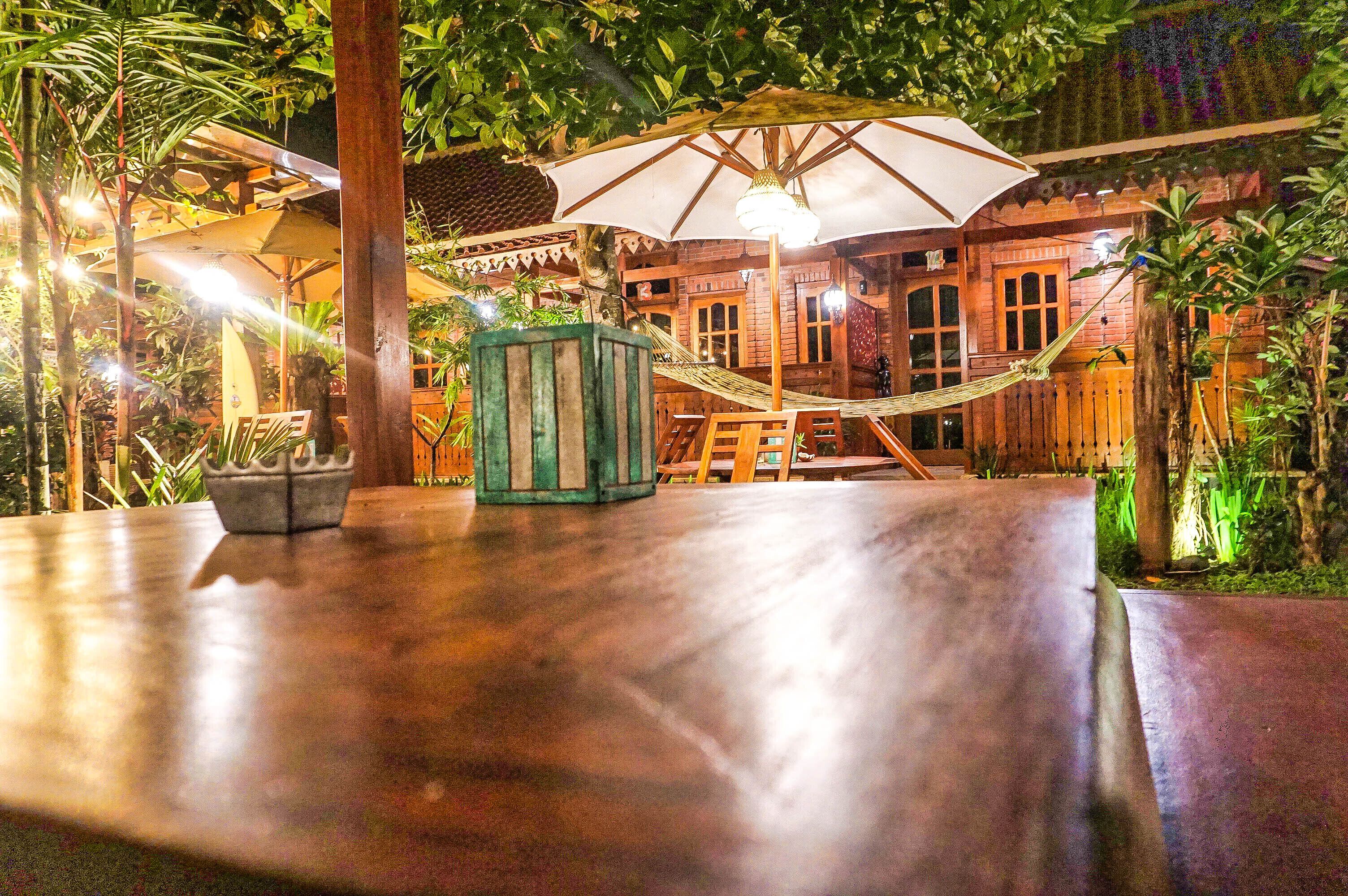 An outdoor seating area with a wooden table, a hammock, and a large umbrella providing shade.