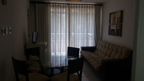 Una sala de estar con una mesa de vidrio, dos sillones, un sofá y un televisor sobre un mueble.