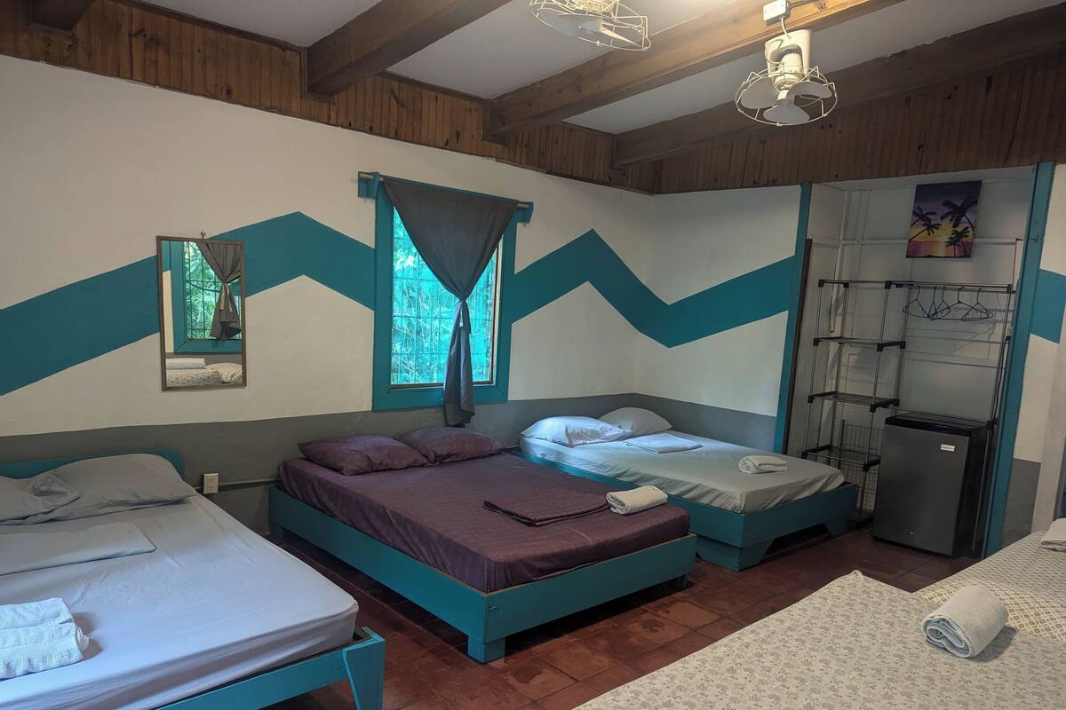 A room with two beds, a small kitchenette, and a mirror.