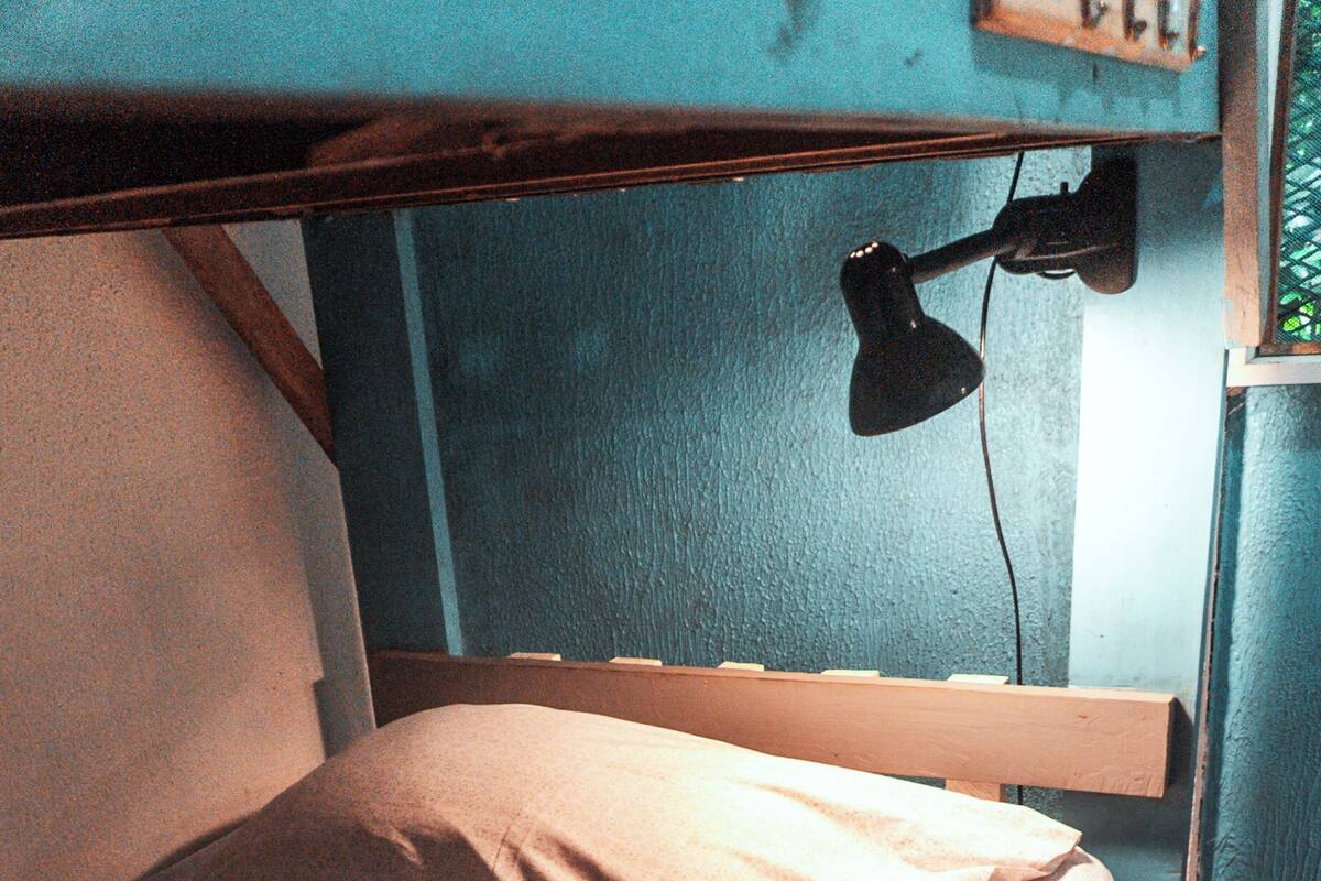 A bunk bed with a single mattress and pillows, a desk with a lamp, and a window with a curtain.