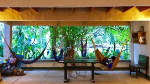 A room with a large window, a hammock, a table, and a bench. - Tasty Dayz Hostel (Cahuita)