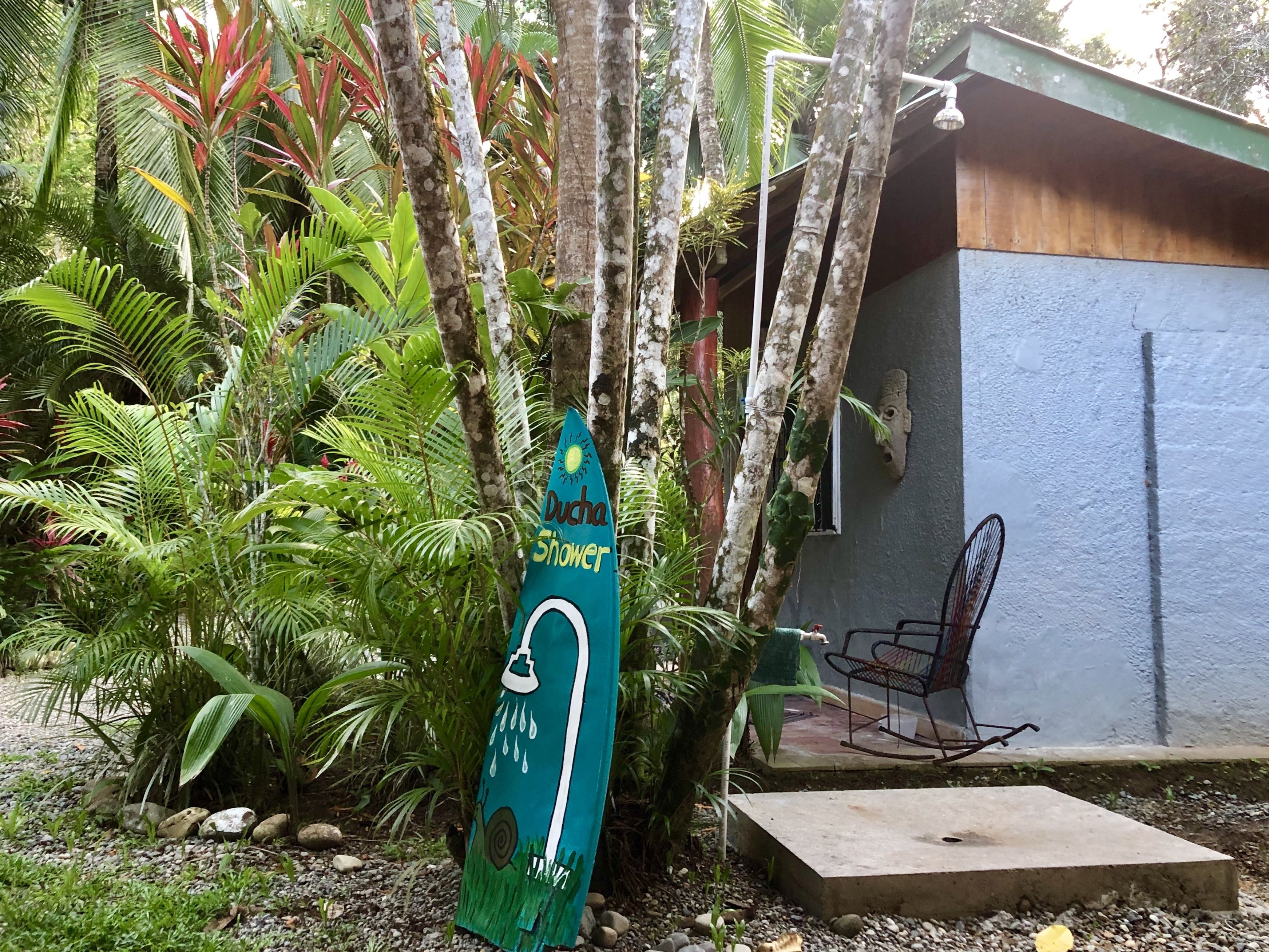 Un jardin tropical avec un panneau indiquant la présence d’une douche, un banc en béton et une structure en bois.