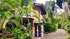 A two-story building with a porch, surrounded by lush tropical vegetation. - Tasty Dayz Hostel (Cahuita)