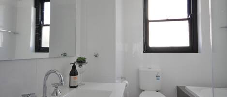 Een moderne badkamer met een witte wastafel, twee kraanwerk, een spiegel, een toilet en een raam.