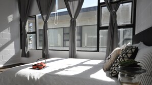 Un dormitorio con cama, cortinas, una ventana y una planta en una mesita de noche.