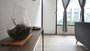 Una sala de estar moderna con un ventanal grande, un sofá gris, una mesita de madera con un jarrón de vidrio que contiene una planta y una alfombra de cuadros en el suelo.
