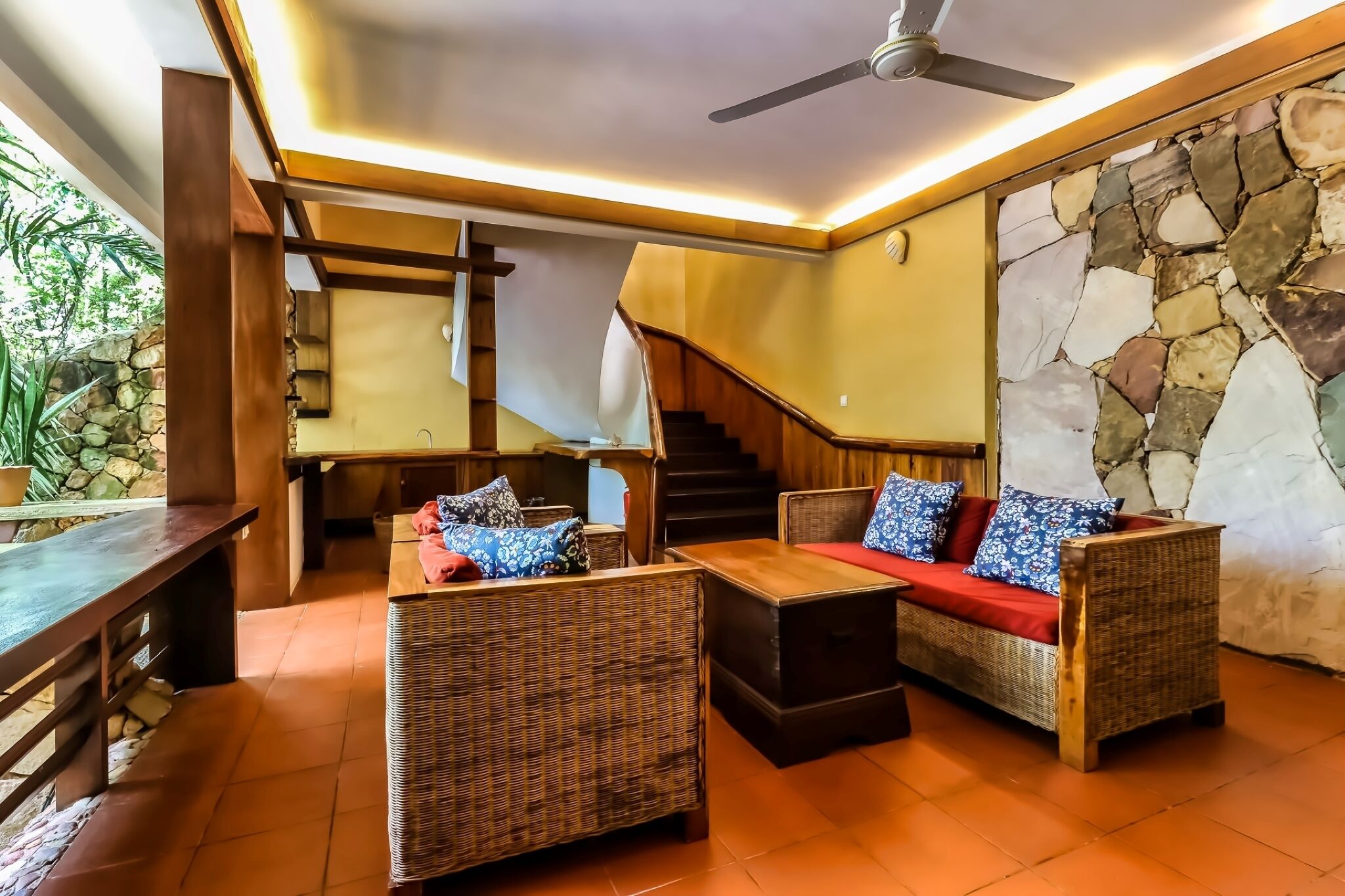 Un espacio interior acogedor con mobiliario de mimbre, un banco de madera y una pared de piedra.