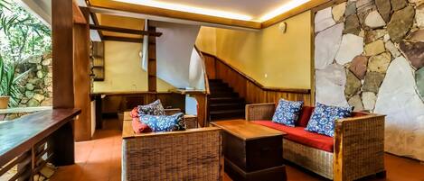Un espacio interior acogedor con mobiliario de mimbre, un banco de madera y una pared de piedra.