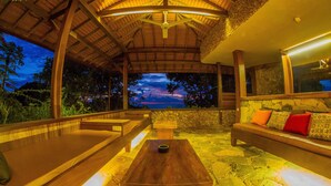 Un espacio al aire libre con mesa y bancos de madera, suelo de piedra y vista al atardecer.