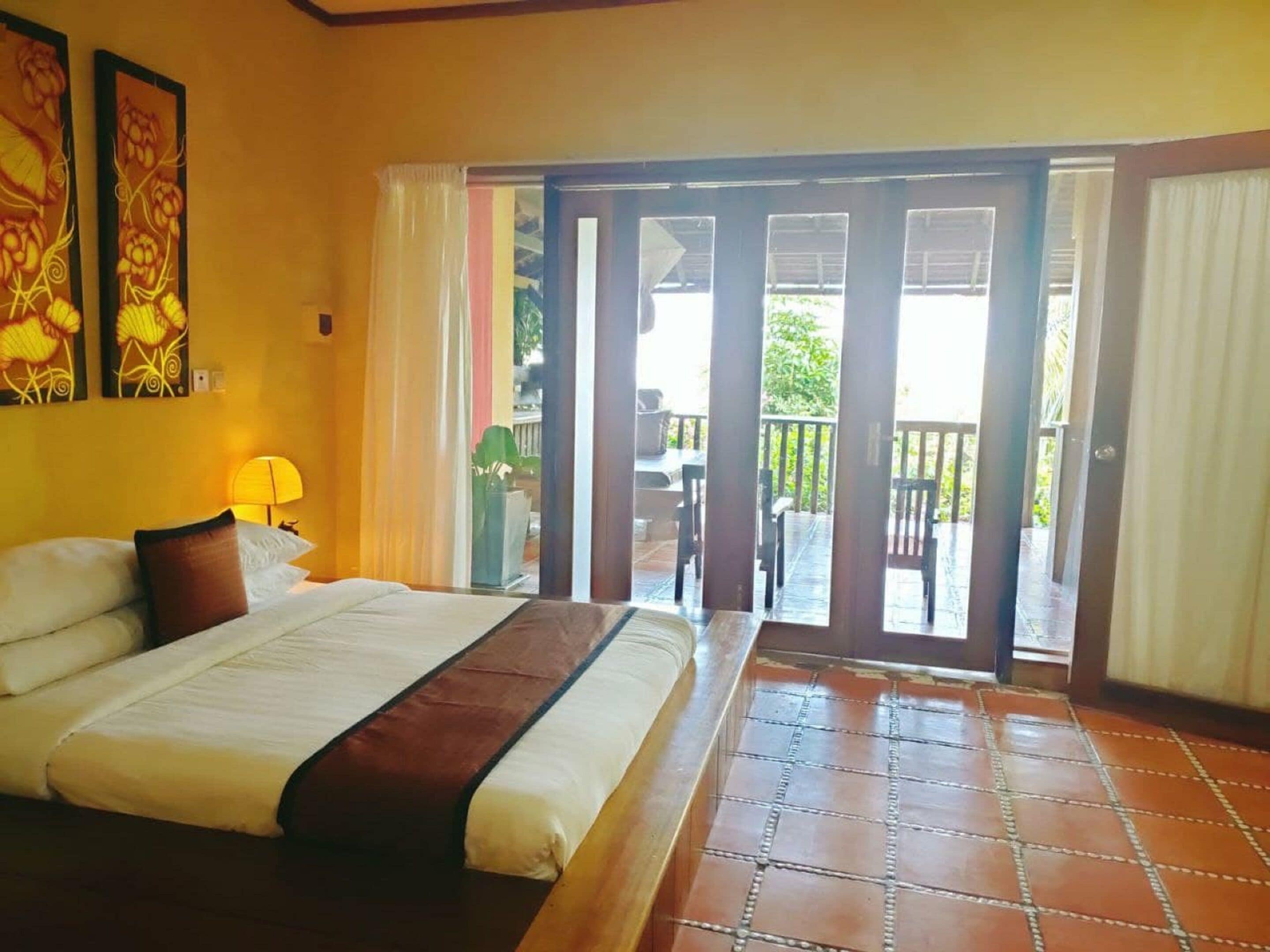 A hotel room with a bed, a nightstand, a lamp, and a view of an outdoor patio area.