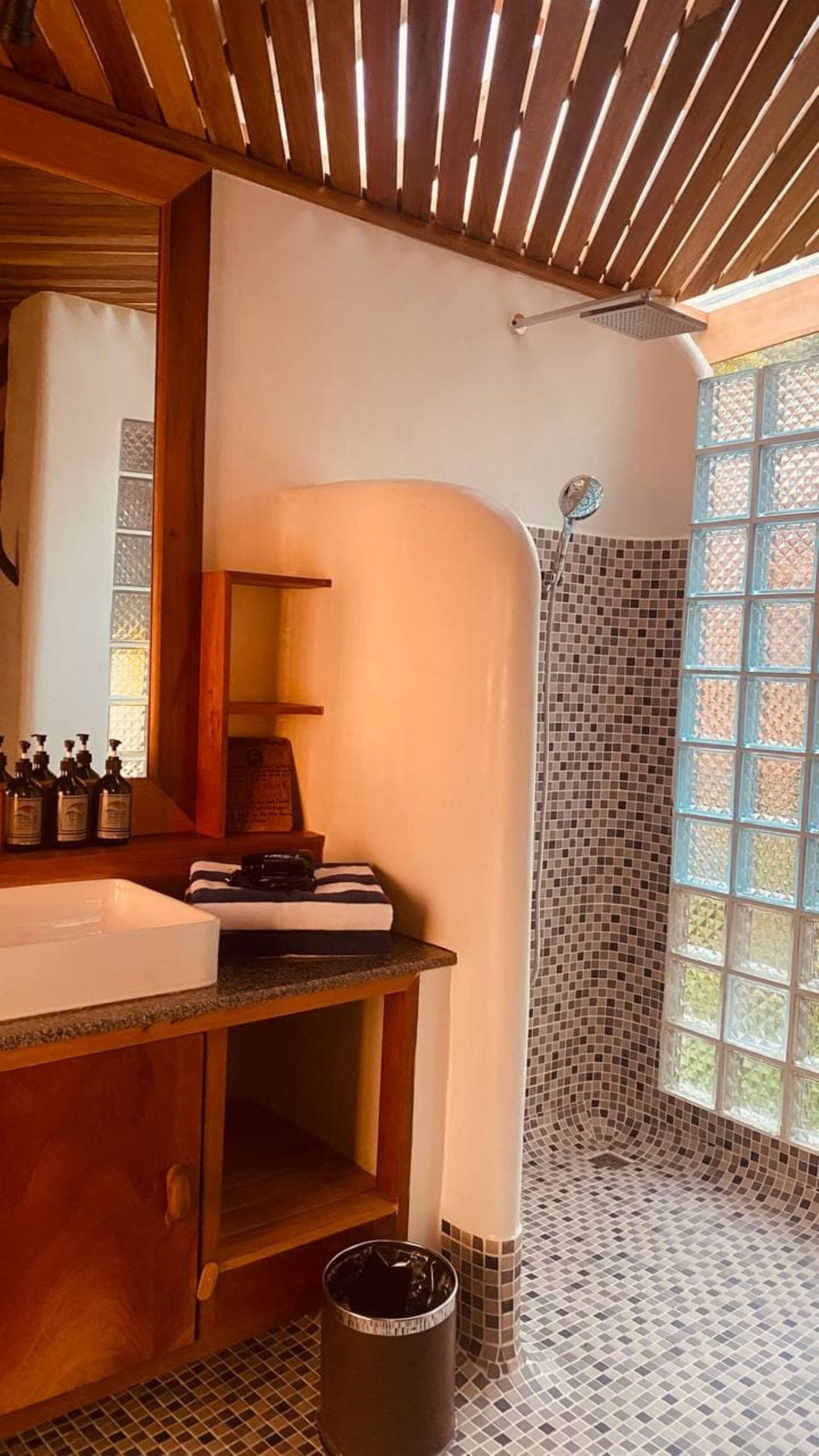 Un baño con tocador de madera, ducha con mosaicos y ventana con vistas.