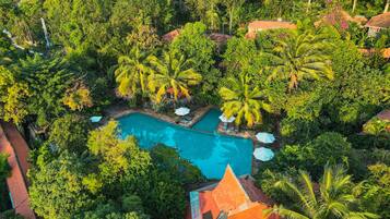 Luchtbeeld van een resort met een zwembad, omgeven door weelderige begroeiing en palmbomen.