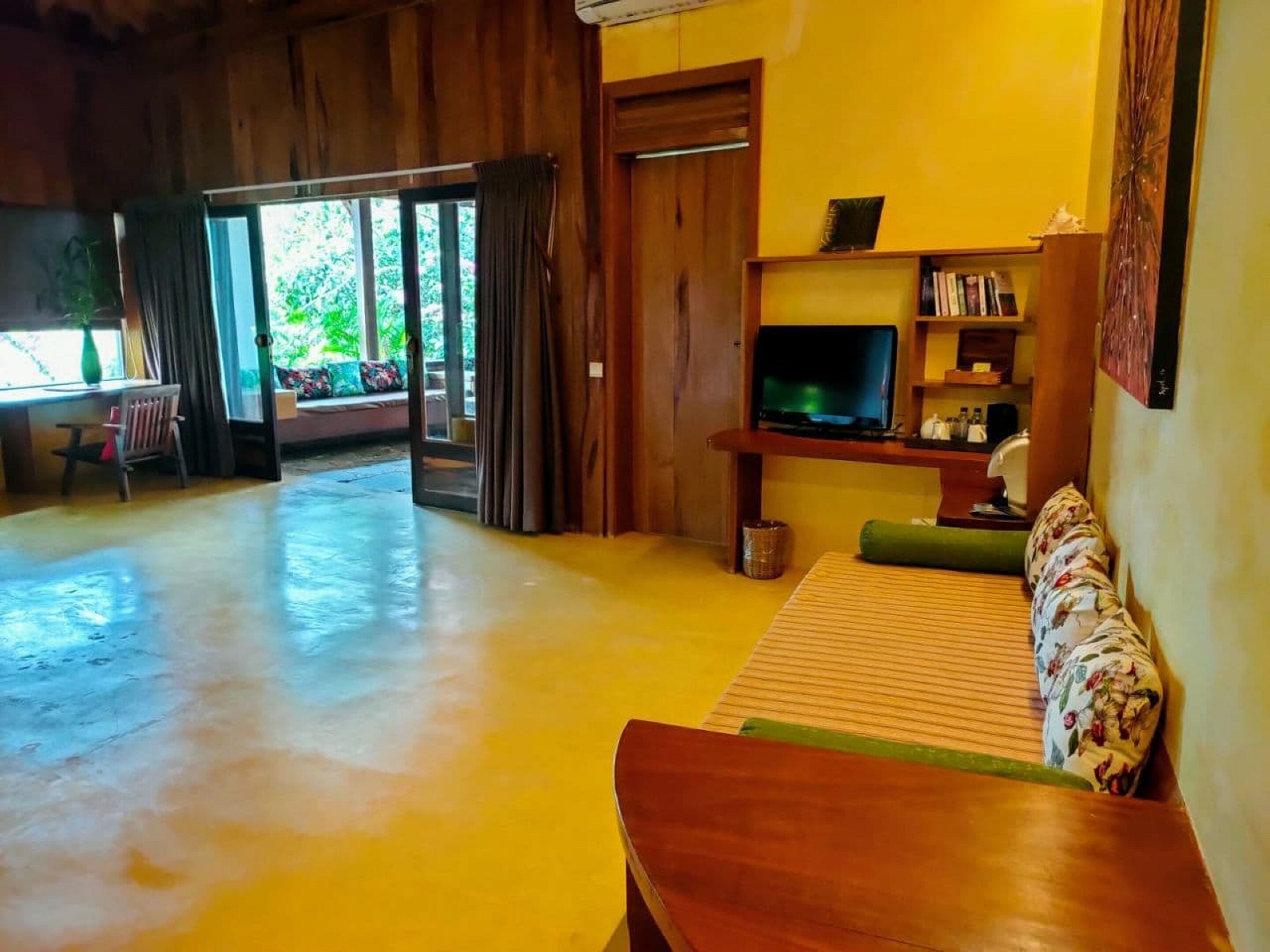 A spacious living area with a wooden floor, a sofa, a television, and a bookshelf.