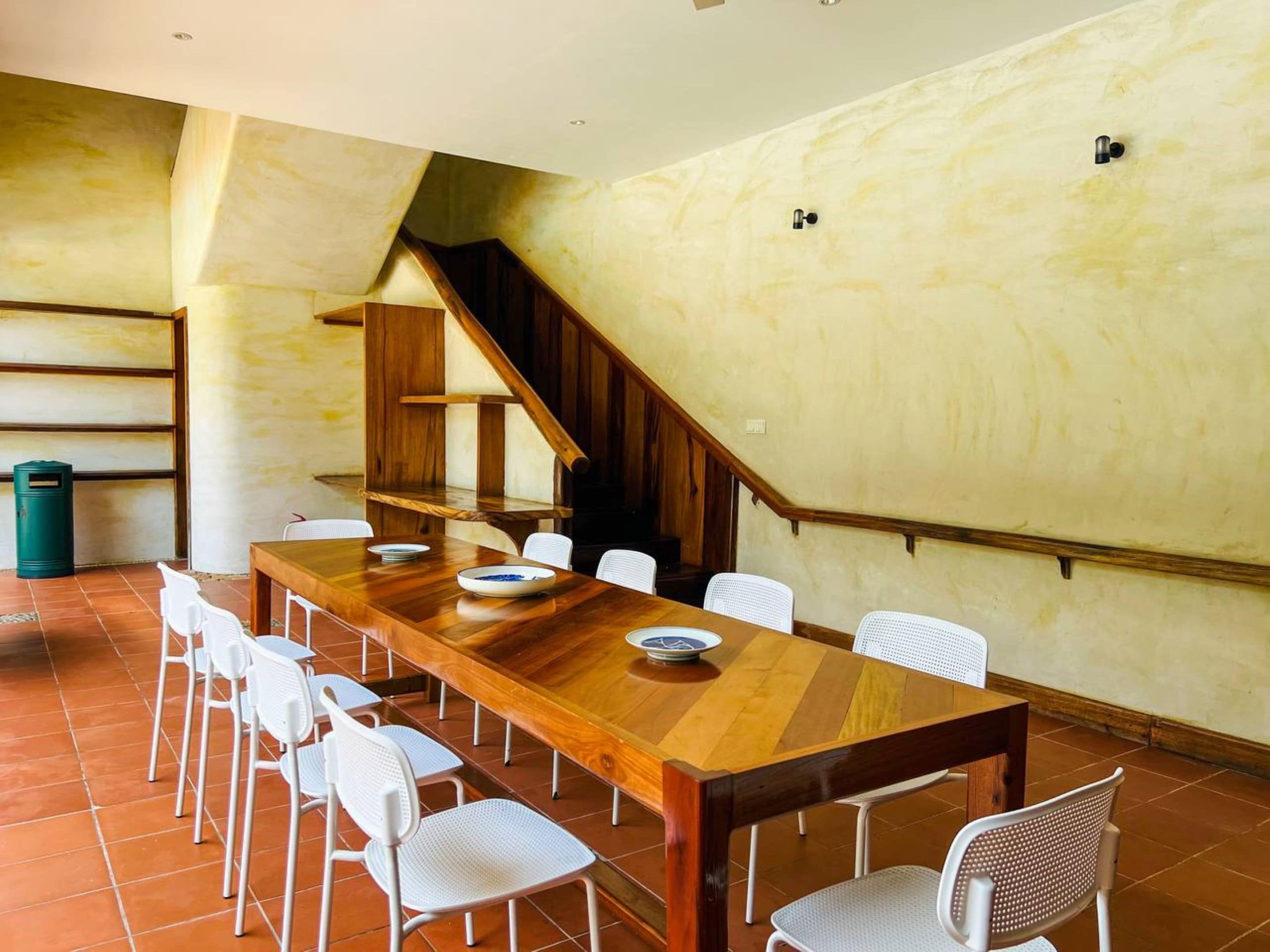 Un comedor con una larga mesa de madera, sillas blancas y una escalera.
