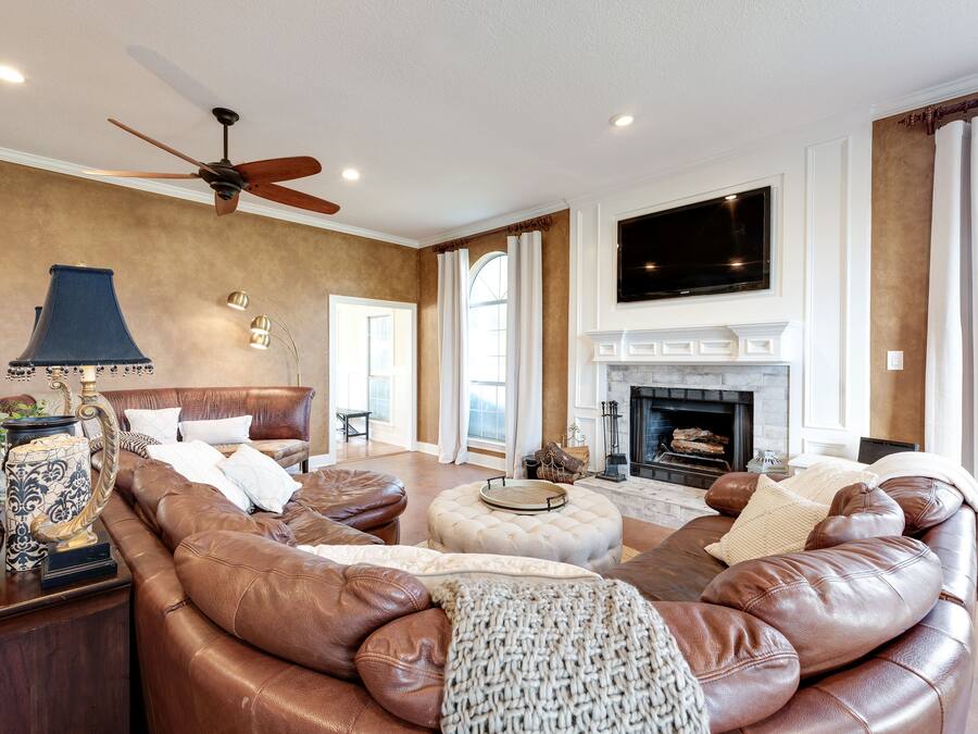 A spacious living room with a leather sofa, a fireplace, a ceiling fan, and a large TV.