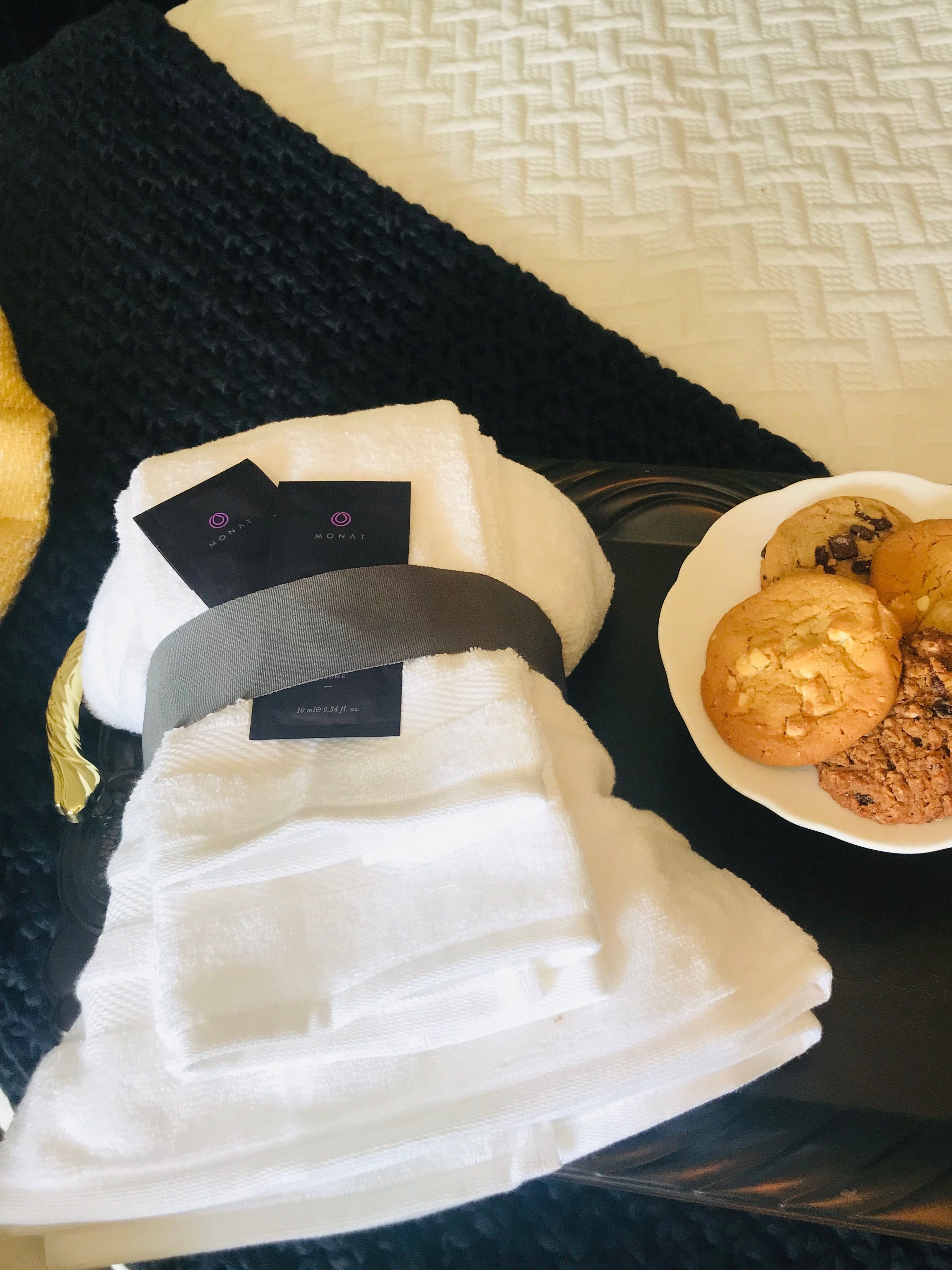 A white towel with a black tag, a plate of cookies, and a black textured blanket on a table.