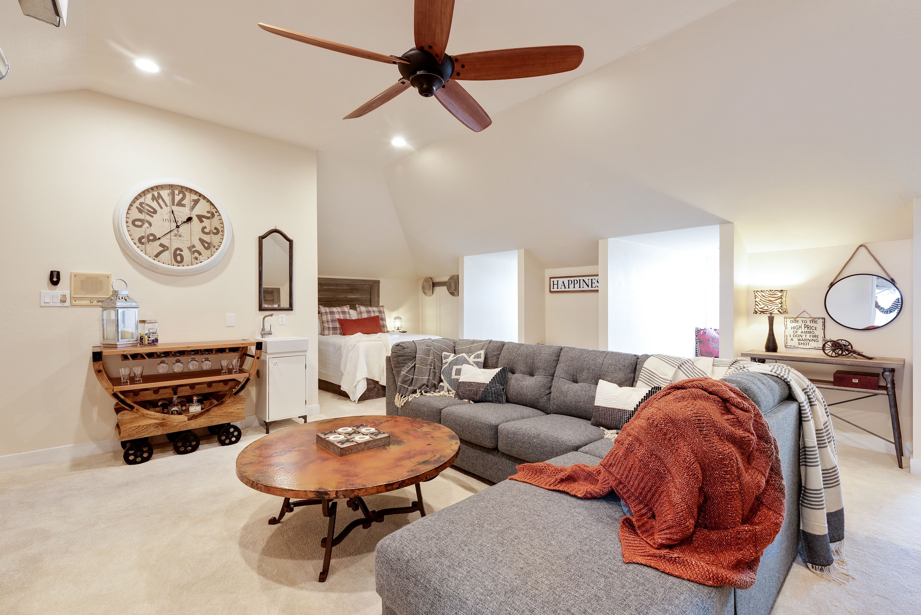 A living room with a ceiling fan, a round clock, a sofa, a coffee table, and a wooden cart with glassware.
