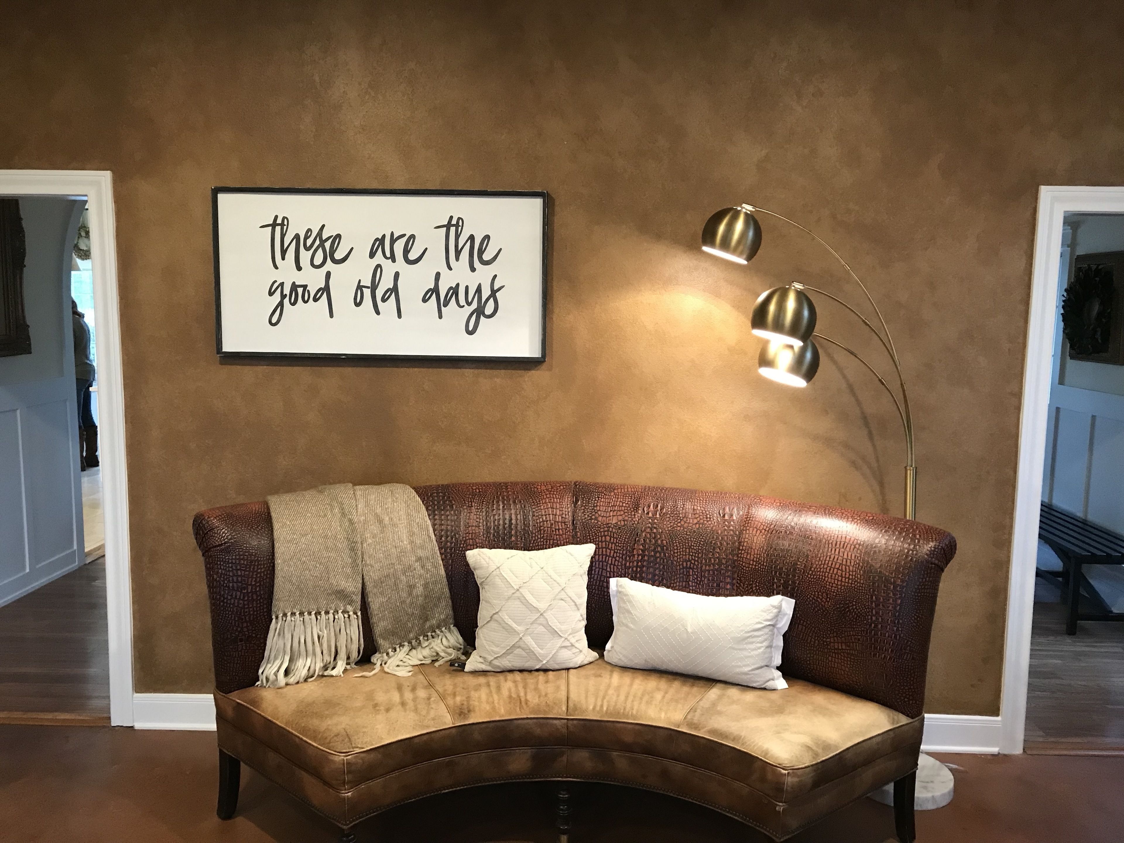 Un sofá de cuero marrón con tres almohadones y una manta, un letrero en la pared y dos lámparas de pie.
