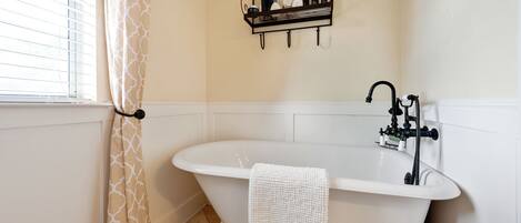 A bathroom with a freestanding bathtub, a towel rack with toiletries, and a window with blinds.