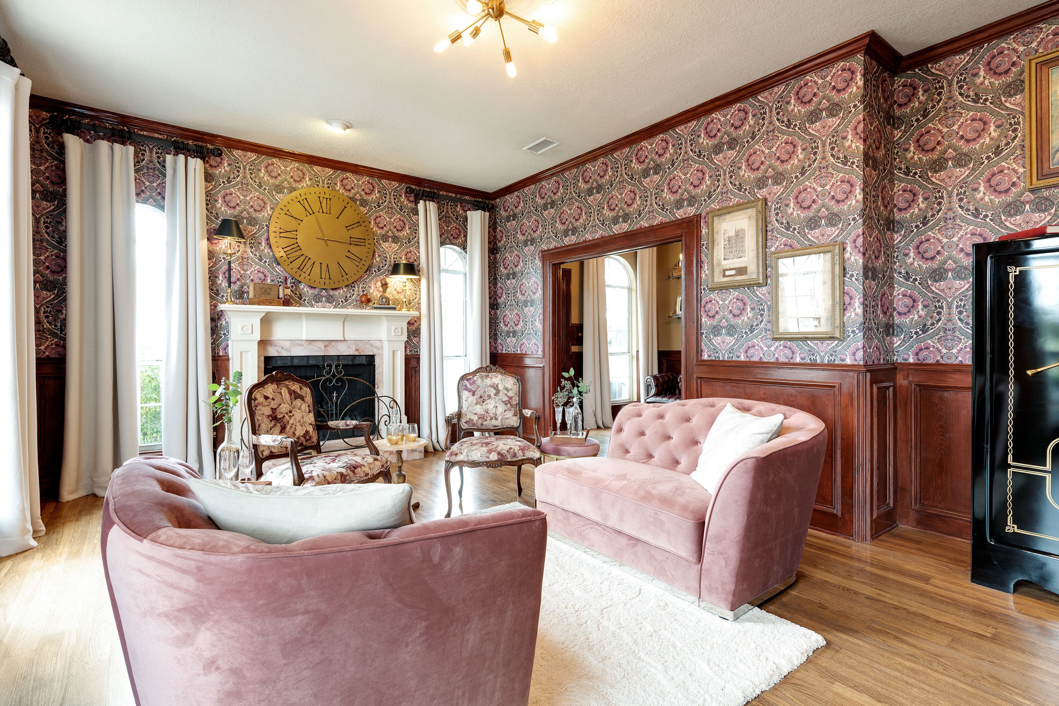 Un salón espacioso con chimenea, dos sillones rosa y un gran reloj en la pared.