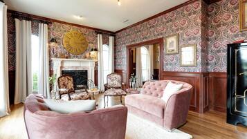 A spacious living room with a fireplace, two pink armchairs, and a large clock on the wall.