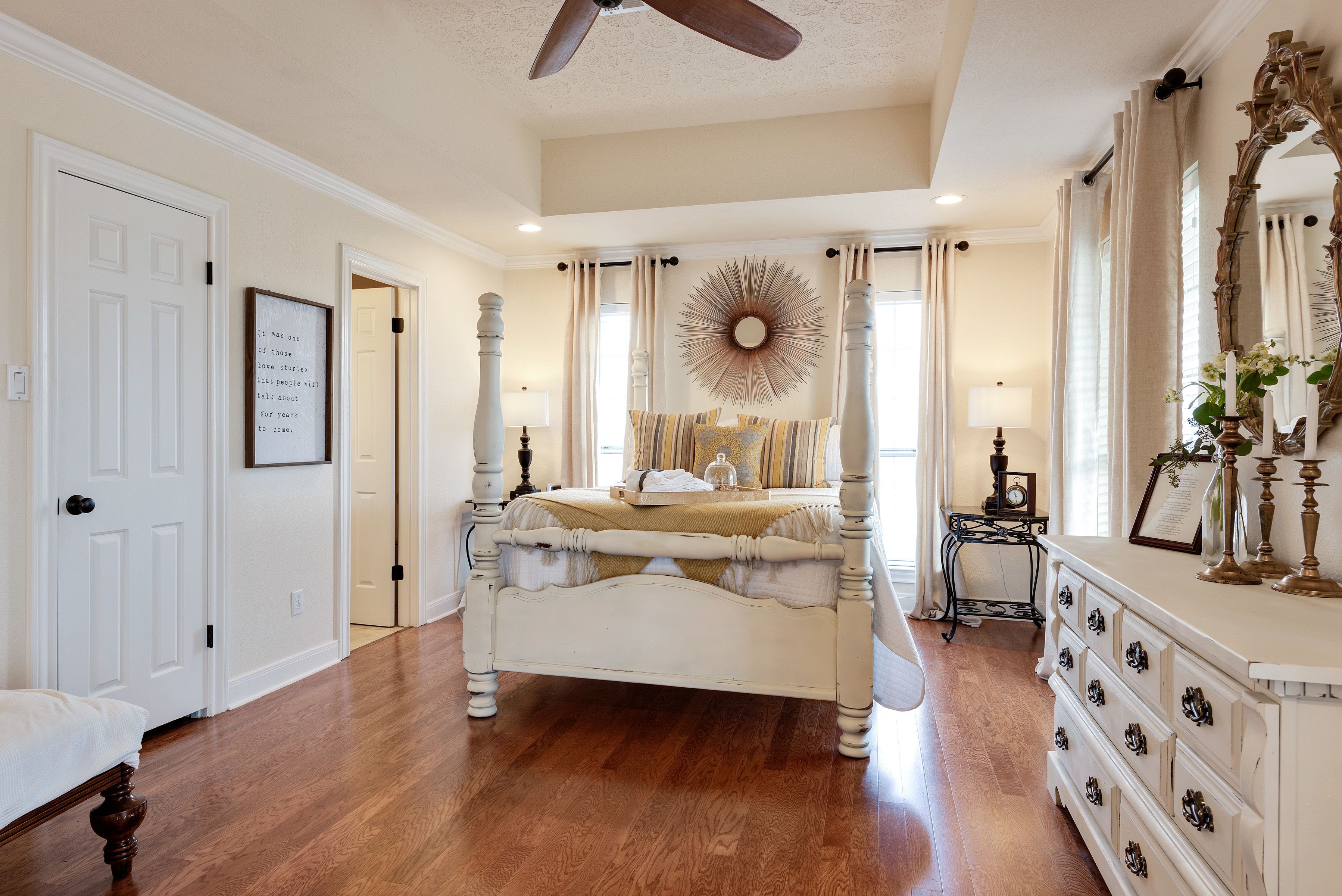 A bedroom with a large bed, a dresser, a mirror, and a ceiling fan.