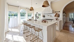 A spacious kitchen with a large island, pendant lights, and a view to the outside.