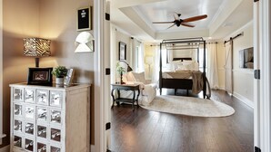 A bedroom with a canopy bed, a ceiling fan, a bedside table with a lamp, and a decorative cabinet.