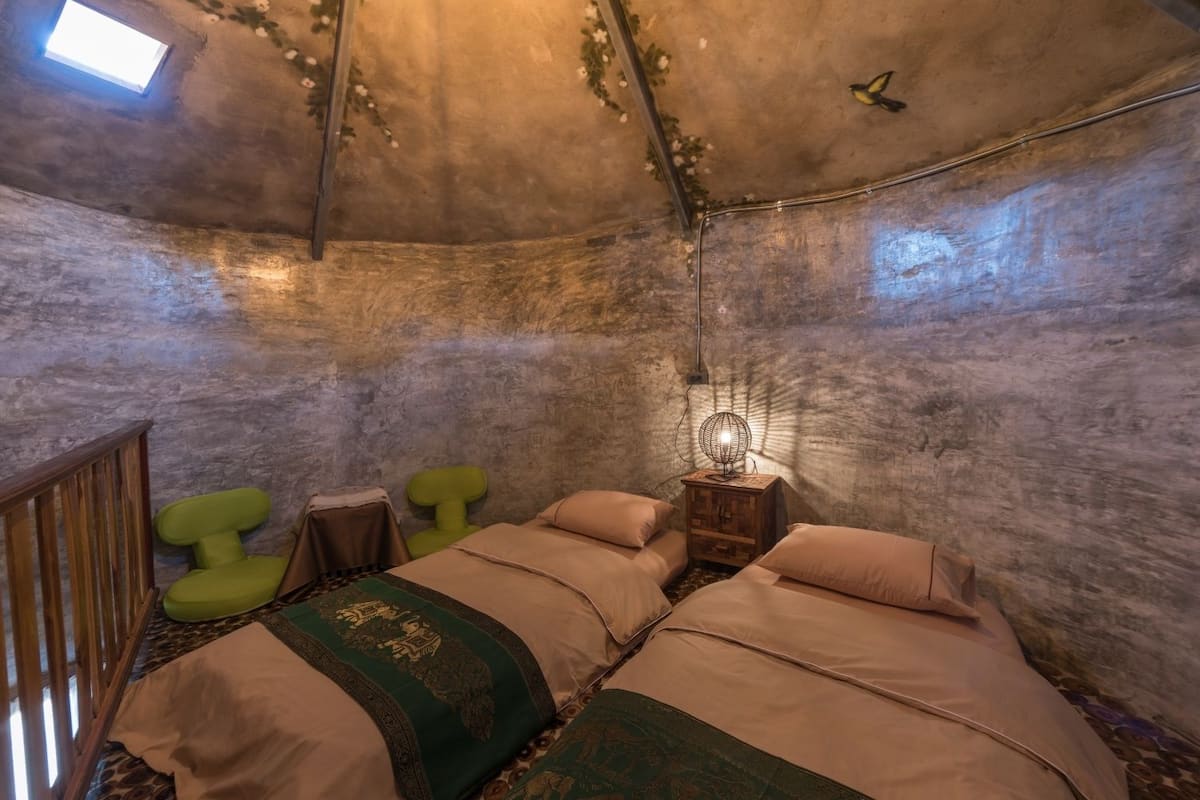 Een knus vertrek met twee bedden, een kleine tafel, een groene stoel en een opvallend bolvormig plafond.