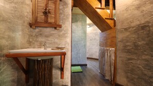 Une salle de bain avec un lavabo en bois, une fenêtre avec des volets et un escalier menant à une autre pièce.