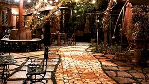 Un espace extérieur aménagé en terrasse, avec un sol en pierre, des tables, des chaises et des guirlandes lumineuses.
