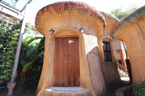 A building with a unique architectural style featuring a wooden door and a small staircase leading to the entrance. - Leafy Greens Clay House (Chiang Mai)