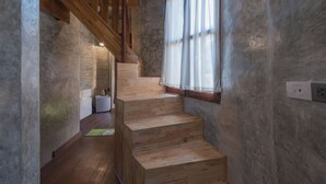 Un escalier en bois dans une pièce avec un mur en béton et une fenêtre ornée de rideaux légers.