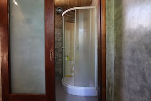 A glass-enclosed shower area with a wooden door frame and a curved ceiling. - Leafy Greens Clay House (Chiang Mai)