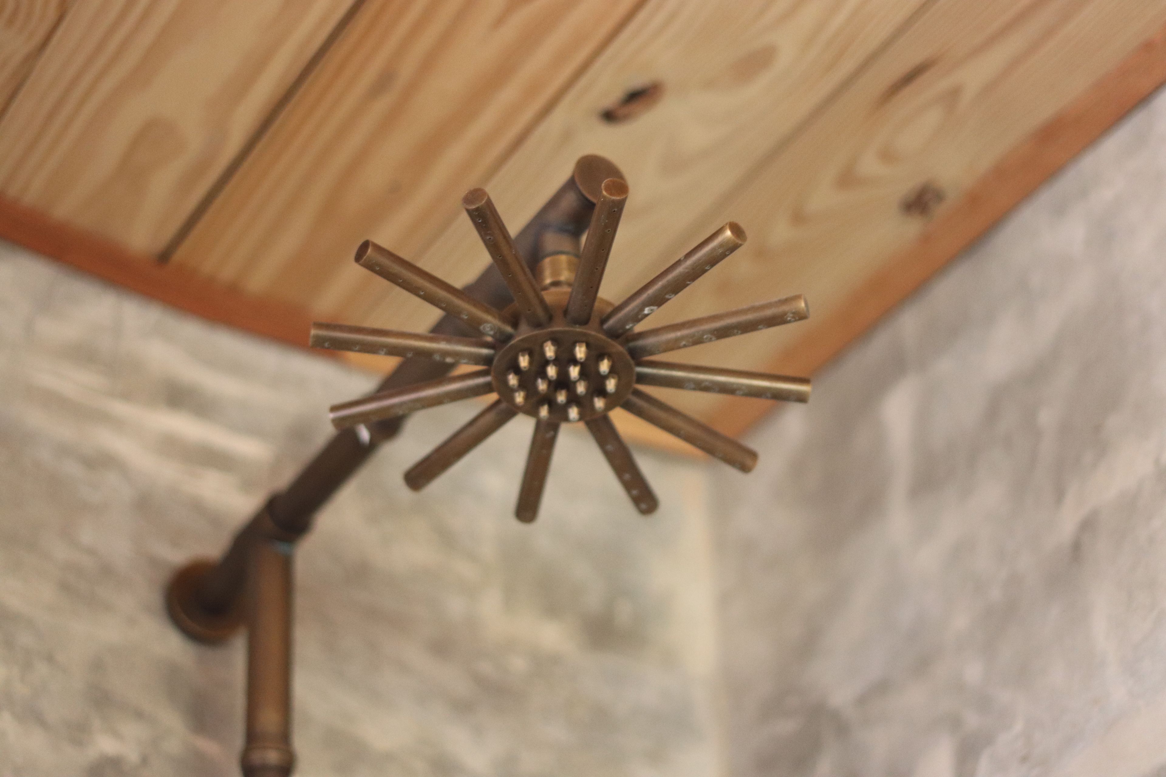 A close-up of a brass ceiling fixture with multiple arms, likely part of a room's lighting or ventilation system.