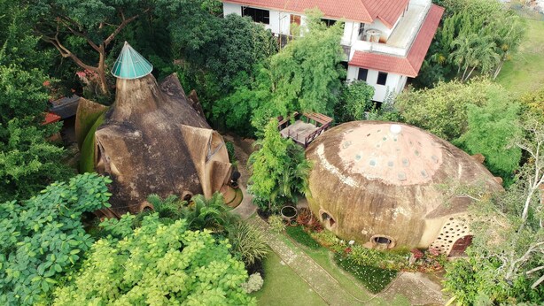Une vue aérienne d’un jardin avec deux grandes structures en forme de dôme, entourées d’une végétation luxuriante, et un bâtiment blanc avec un toit rouge en arrière-plan.