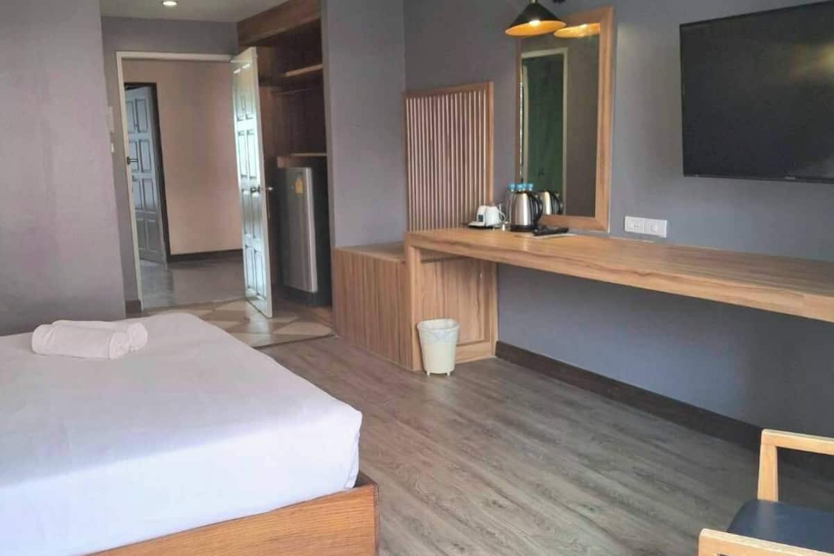 A modern hotel room with a bed, a small table, a TV, and a kitchenette area.