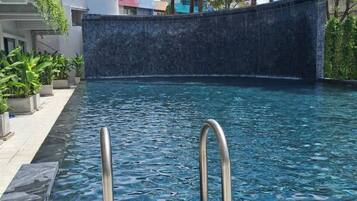 A swimming pool with clear water, surrounded by a stone wall and potted plants.