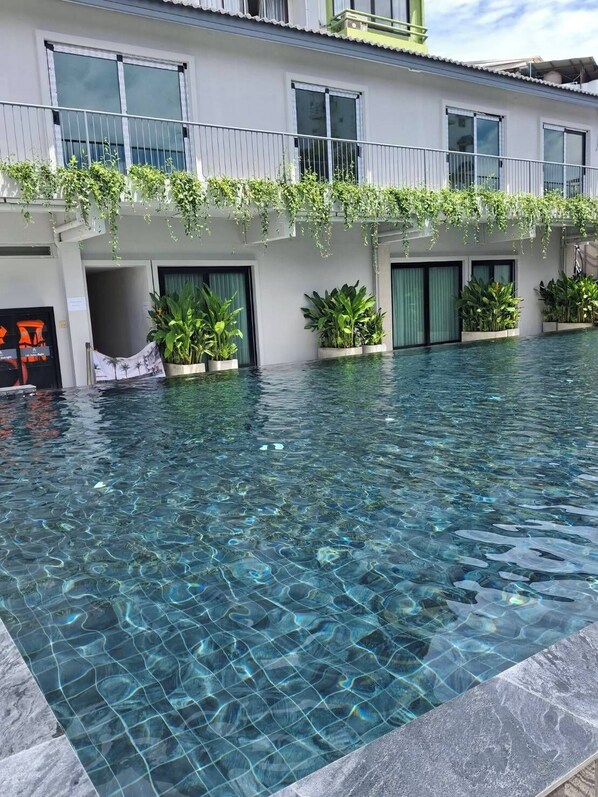 Una piscina cristalina con borde de azulejos, rodeada por un edificio con varias ventanas y plantas en macetas.