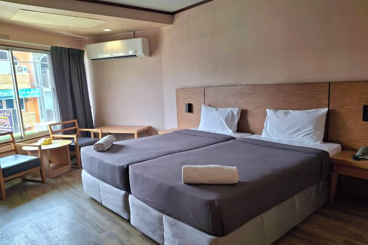 A hotel room with two beds, a small table, a chair, and an air conditioning unit.