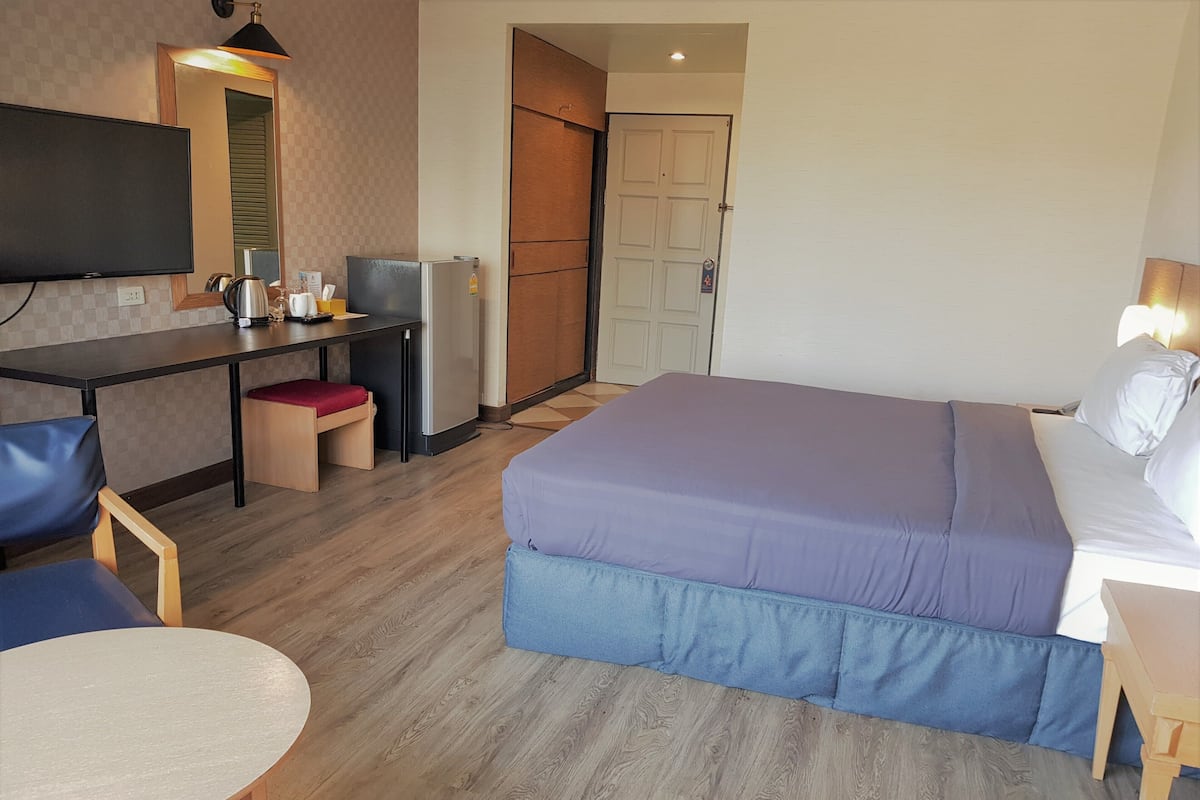 A hotel room with a bed, a desk with a chair, a small table, a refrigerator, and a television.