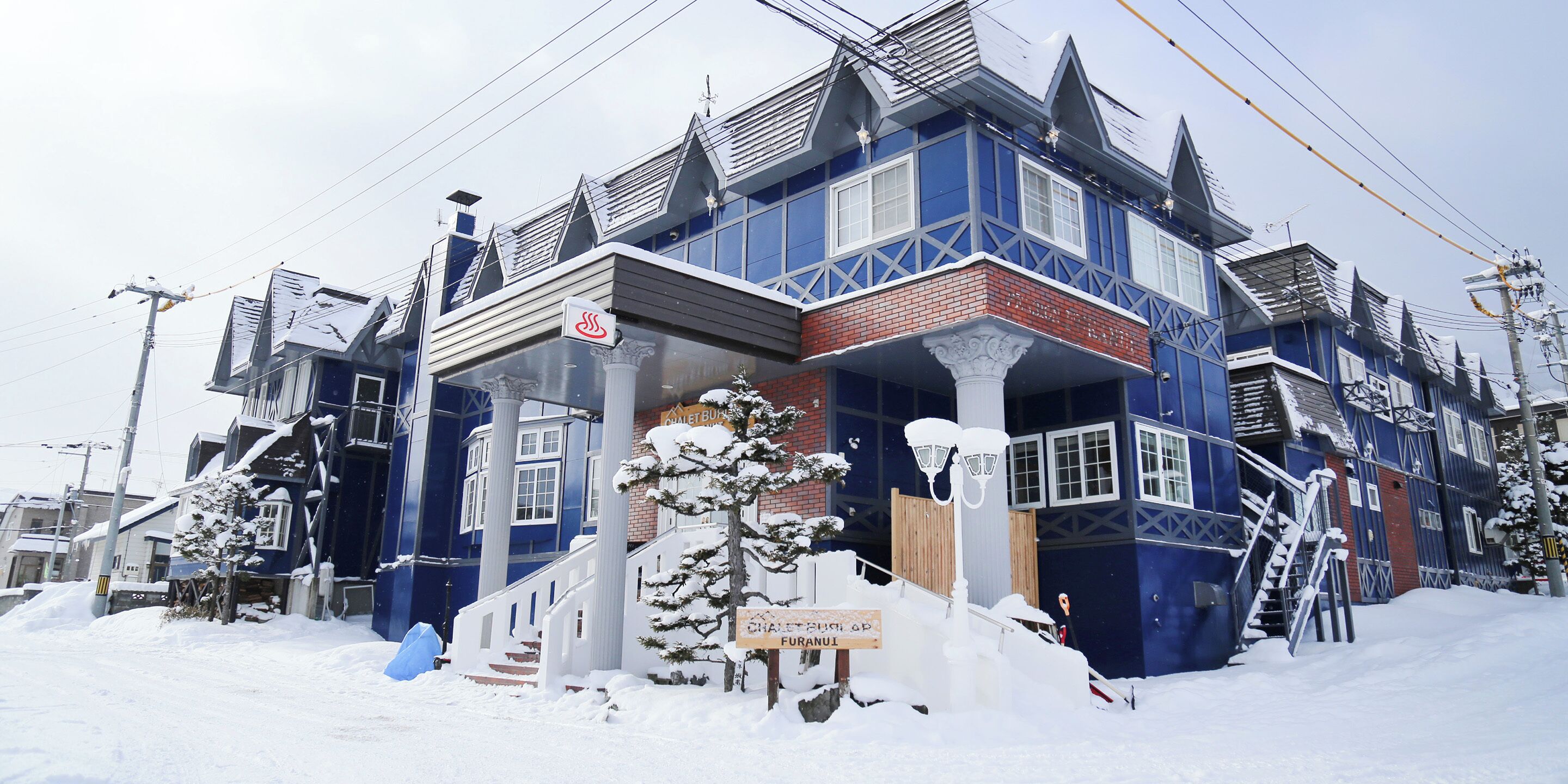 A snow-covered building with a blue facade, a wooden staircase, and a sign indicating a sauna.