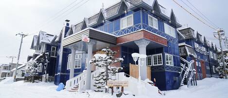 Edificio cubierto de nieve con fachada azul, una escalera de madera y un cartel que indica una sauna.