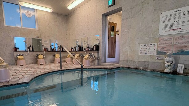 Une piscine avec un revêtement intérieur en carrelage, un vestiaire doté de miroirs et un espace d’accueil comprenant un comptoir et divers objets.