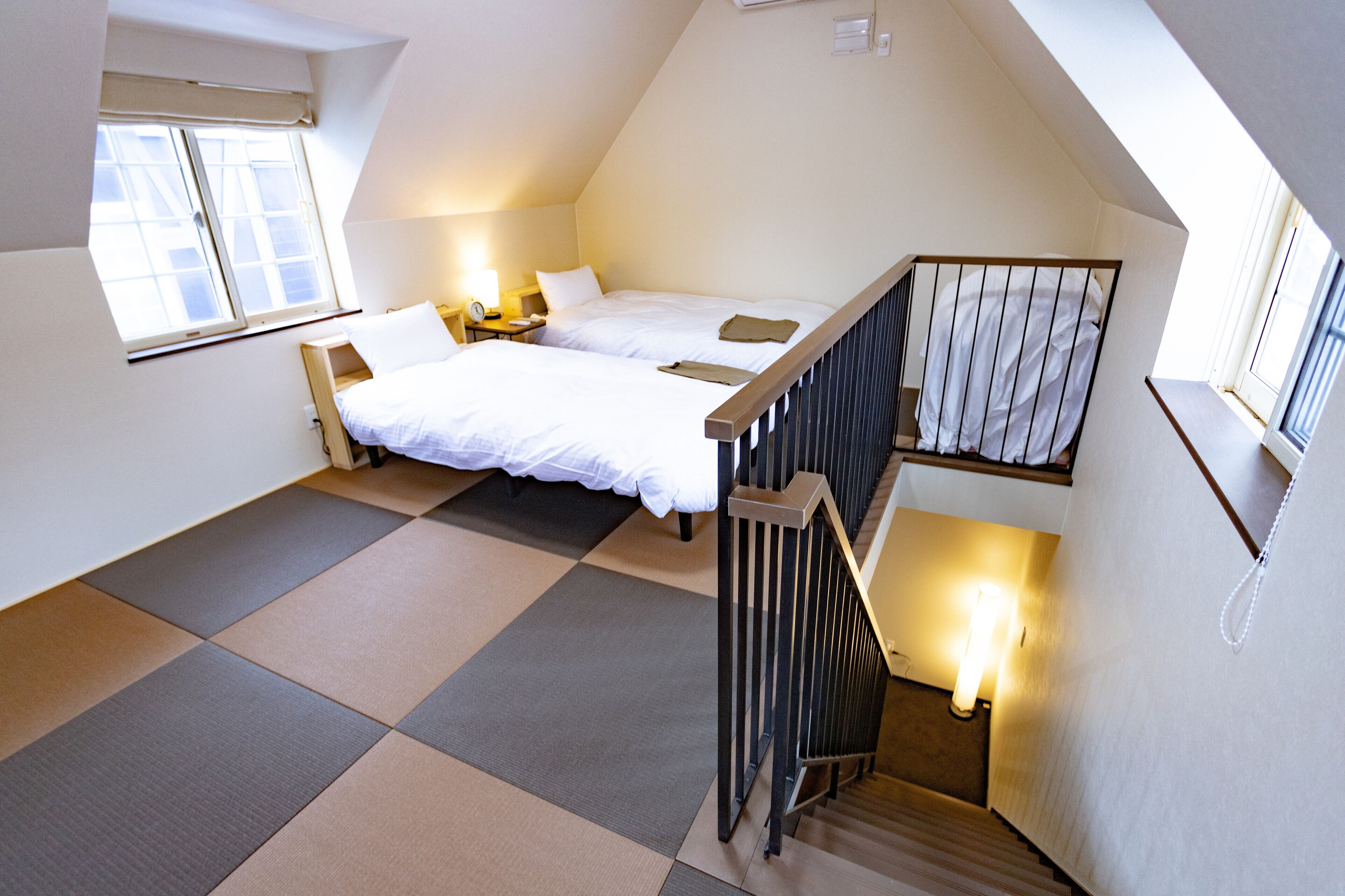 A bedroom with two beds, a wooden staircase, and a window.