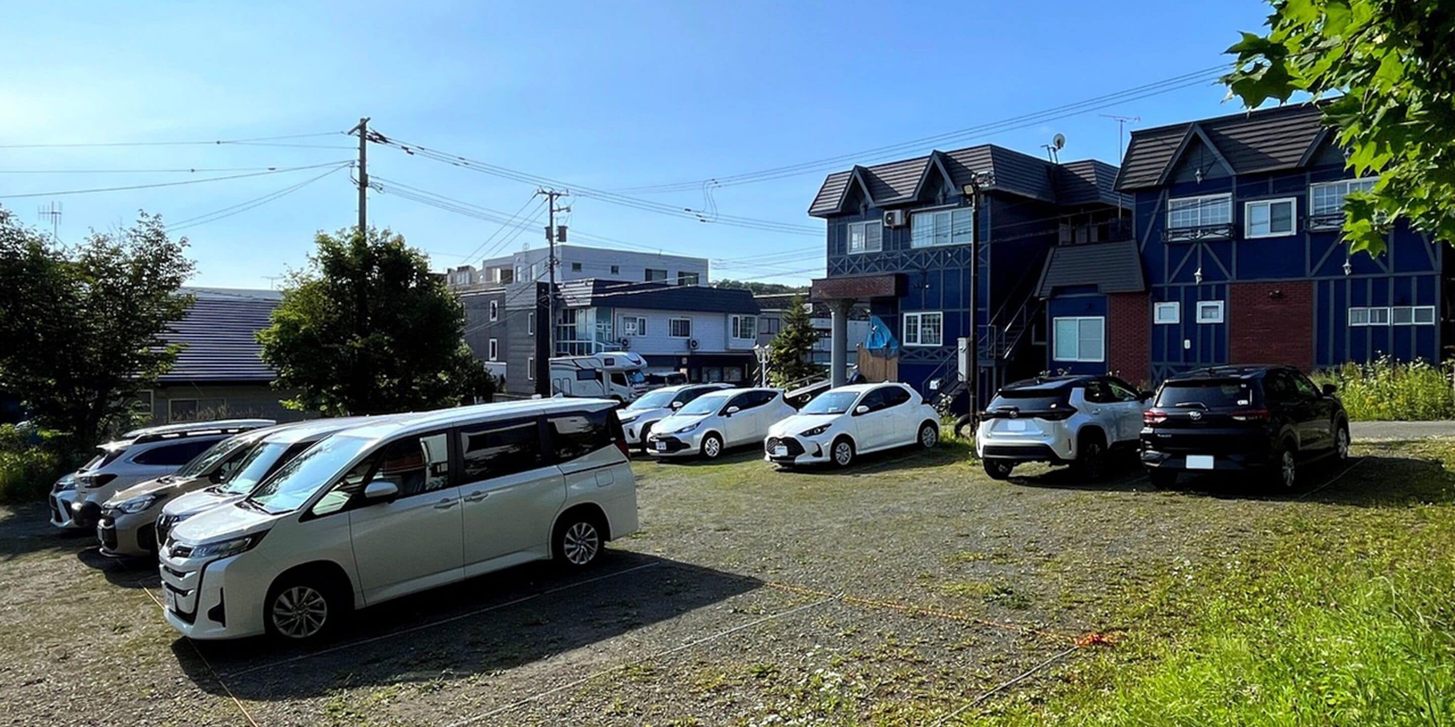 Un estacionamiento con varios autos y un edificio de fachada oscura y múltiples ventanas.